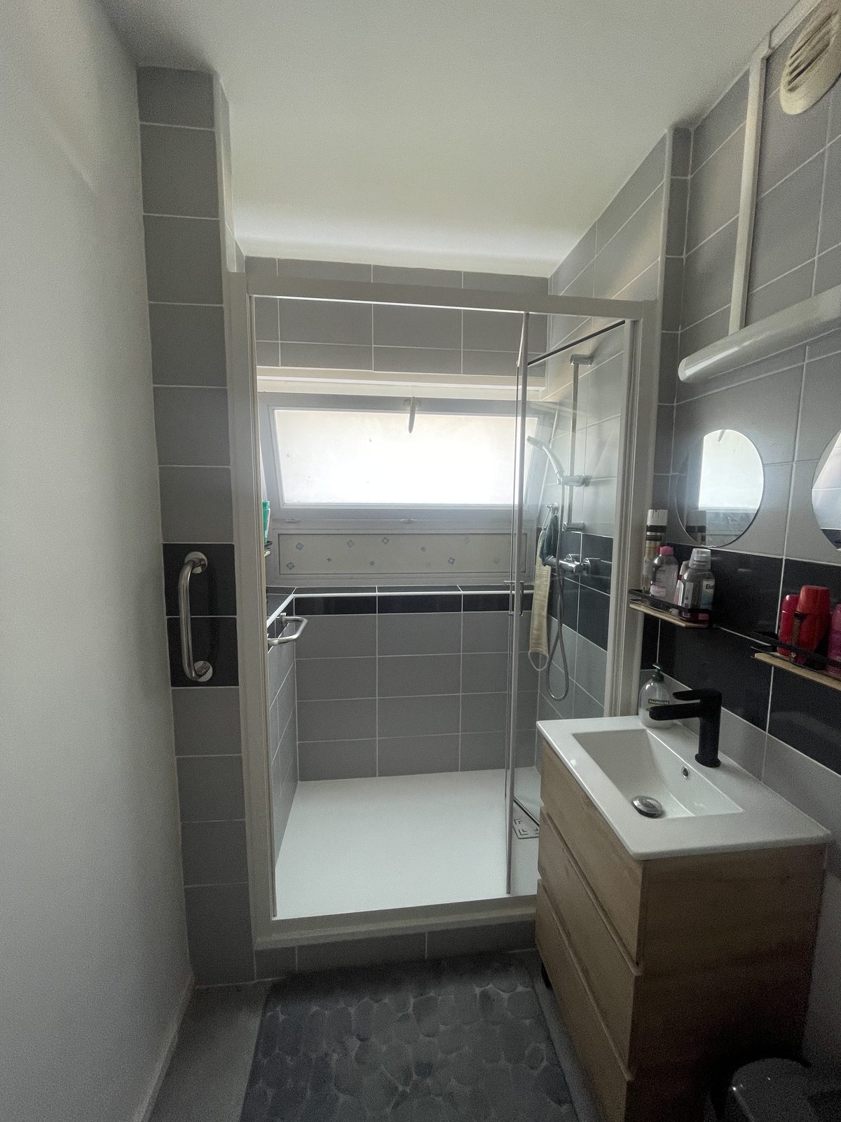 La même salle d'eau après rénovation : espace douche, faïence grise et meuble vasque bois